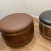 Two barrel-shaped stools, one brown and one with a black top and wooden sides, on a wooden floor.